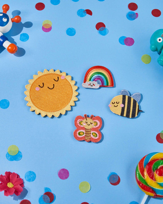 Spring Friends swappable backpack patches with bee, rainbow, butterfly and sun designs displayed on a colourful floral background